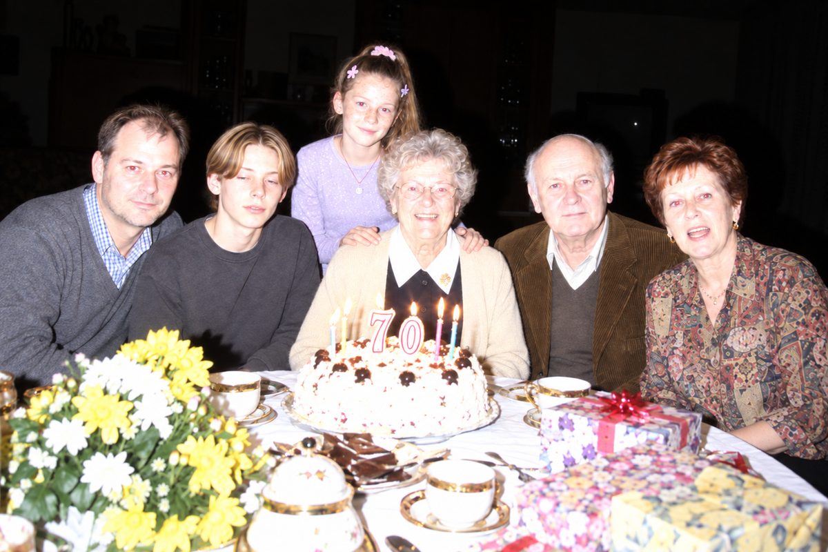 the family at the birthday table: thomas, philip, julia, grandma gerda and the beckers from next door, behind a cake with a 70.